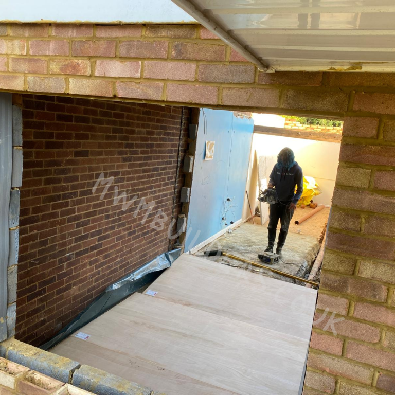 Garage Conversions A person standing on a wooden frame in a partially garage conversion space.
